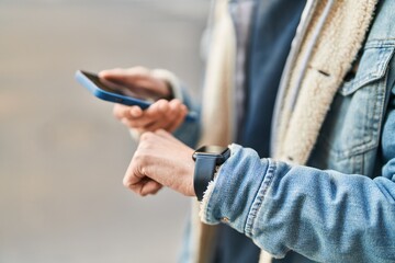 Young hispanic man using smartphone and watch at street