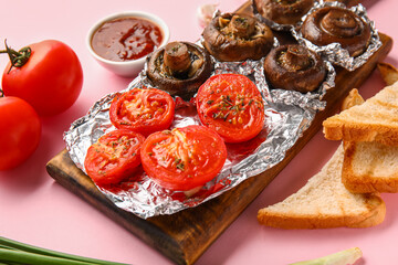 Wooden board with tasty baked mushrooms, tomatoes, sauce and toasts on pink background, closeup