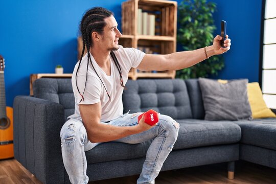 Young man training with dumbbell make selfie by smartphone at home
