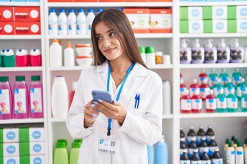 Young beautiful hispanic woman pharmacist using smartphone working at pharmacy