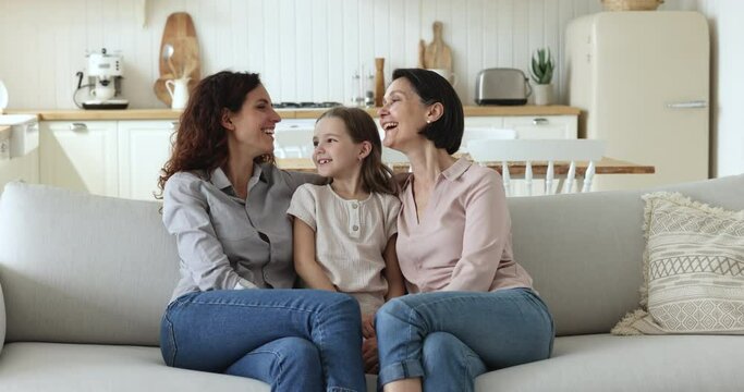 Cheerful girls and women of three female generations meeting at home, sitting close in couch, hugging with affection, talking, chatting, laughing, enjoying family leisure, bonding, relationship