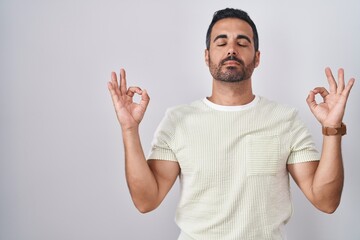 Hispanic man with beard standing over isolated background relaxed and smiling with eyes closed...