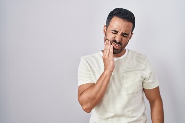 Hispanic man with beard standing over isolated background touching mouth with hand with painful expression because of toothache or dental illness on teeth. dentist