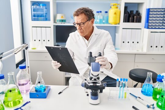 Middle age man wearing scientist uniform using microscope at laboratory
