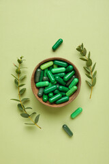 Bowl with capsules and plant branches on green background