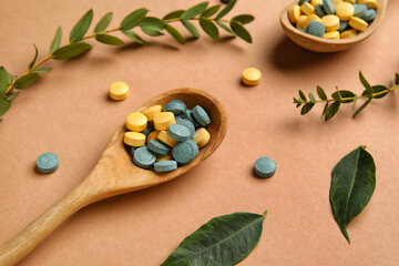 Spoons with pills and plant branches on beige background, closeup