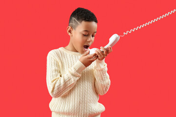 Little African-American boy talking by telephone on red background