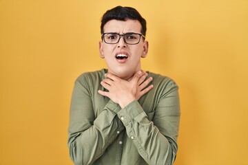 Obraz premium Non binary person standing over yellow background shouting and suffocate because painful strangle. health problem. asphyxiate and suicide concept.