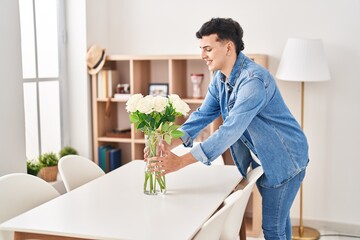 Young non binary man smiling confident putting flowers on table at home