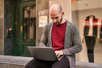 Young man using laptop sitting on bench at street