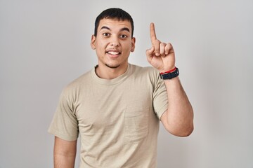 Young arab man wearing casual t shirt pointing finger up with successful idea. exited and happy. number one.