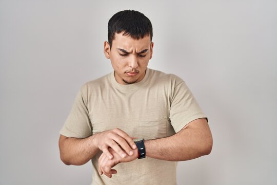 Young arab man wearing casual t shirt checking the time on wrist watch, relaxed and confident
