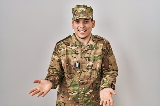 Young arab man wearing camouflage army uniform smiling cheerful with open arms as friendly welcome, positive and confident greetings