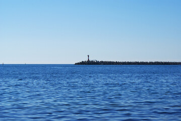 View of the lighthouse in the sea, resort embankment, sun glare on the water, background