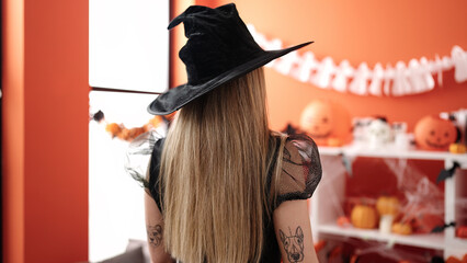 Young blonde woman wearing witch costume standing on back view at home