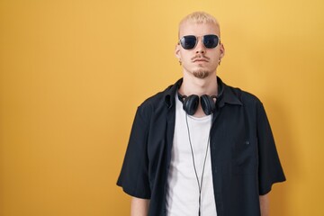 Young caucasian man wearing sunglasses standing over yellow background relaxed with serious expression on face. simple and natural looking at the camera.
