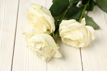 Roses with engagement ring on white wooden background, closeup