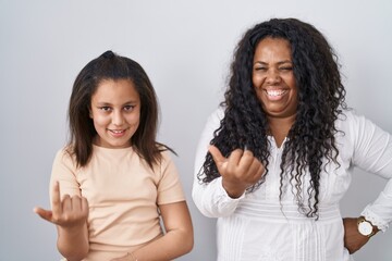 Mother and young daughter standing over white background beckoning come here gesture with hand inviting welcoming happy and smiling