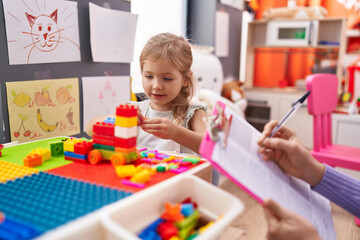 Fototapeta premium Adorable blonde girl playing with construction blocks having therapy at kindergarten