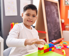 Adorable hispanic boy playing with construction blocks sitting on table at kindergarten