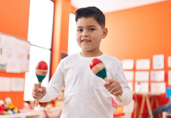 Adorable hispanic boy smiling confident playing maraca at kindergarten