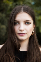 Closeup portrait of a beautiful girl with green eyes and make-up, looking at camera, isolated tree background.