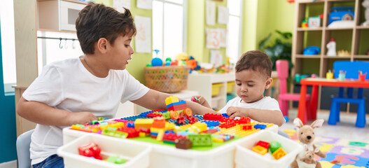 Fototapeta premium Adorable boys playing with construction blocks sitting on table at kindergarten