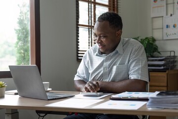 Fototapeta premium African American man calculating using machine managing household finances at home, focused biracial male make calculations on calculator account taxes or expenses