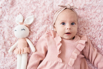 Adorable caucasian baby lying on bed with doll at bedroom