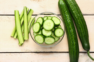 Bowl with cut and whole cucumbers on light wooden background