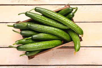 Box with fresh cucumbers on light wooden background