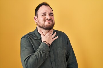 Obraz premium Plus size hispanic man with beard standing over yellow background touching painful neck, sore throat for flu, clod and infection