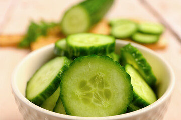 Bowl with fresh cut cucumber on light wooden background, closeup