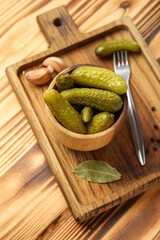 Bowl with tasty fermented cucumbers, board and ingredients on wooden background