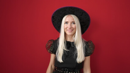 Young blonde woman wearing witch costume smiling confident over isolated red background