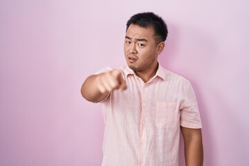 Chinese young man standing over pink background pointing displeased and frustrated to the camera,...