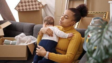 Mother and son tired sitting on sofa holding baby at new home