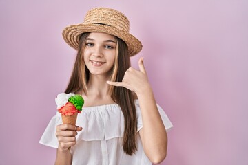 Teenager girl holding ice cream smiling doing phone gesture with hand and fingers like talking on the telephone. communicating concepts.