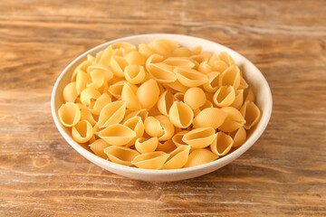Bowl with raw conchiglie pasta on wooden background