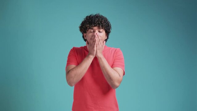 young Indian handsome man looking happy and excited, shocked with an unexpected surprise with both hands open next to face on blue studio background