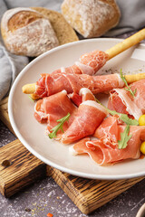 Plate with slices of tasty jamon and Italian Grissini on table, closeup