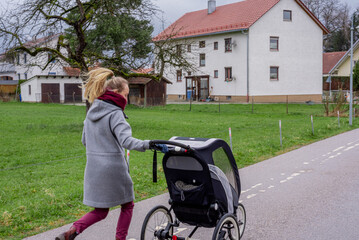 Young active woman jogging with her baby in a stroller. Back view.