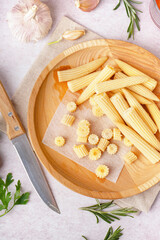 Plate with cut and whole canned baby corn cobs on light background