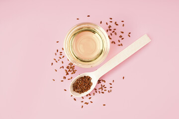 Bowl with flax oil and spoon of seeds on pink background