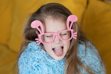 Cute little child girl  in blue fluffy coat wearing bunny ears glasses a on Easter day. Easter girl portrait, funny emotions, surprise..