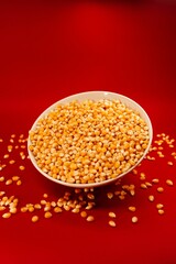 Vertical closeup of a popcorn bowl with some corns spilled around it isolated on a red background
