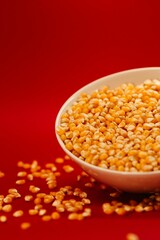 Vertical closeup of a popcorn bowl with some corns spilled around it isolated on a red background