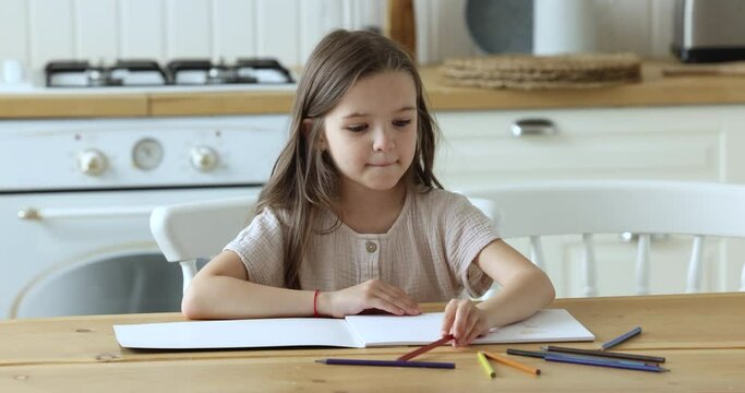 Focused cute primary school kid drawing in pencils in album at home. Serious pretty girl engaged in home activities, learning game, scratching doodles on paper, training creativity