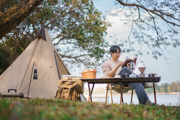 Camping concept, Man camping near lake and sitting outside tent to relaxation with reading a book