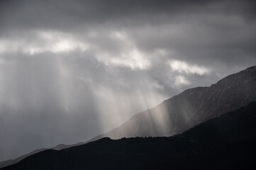 Dark dramatic sky with light rays and mountains silhouettes